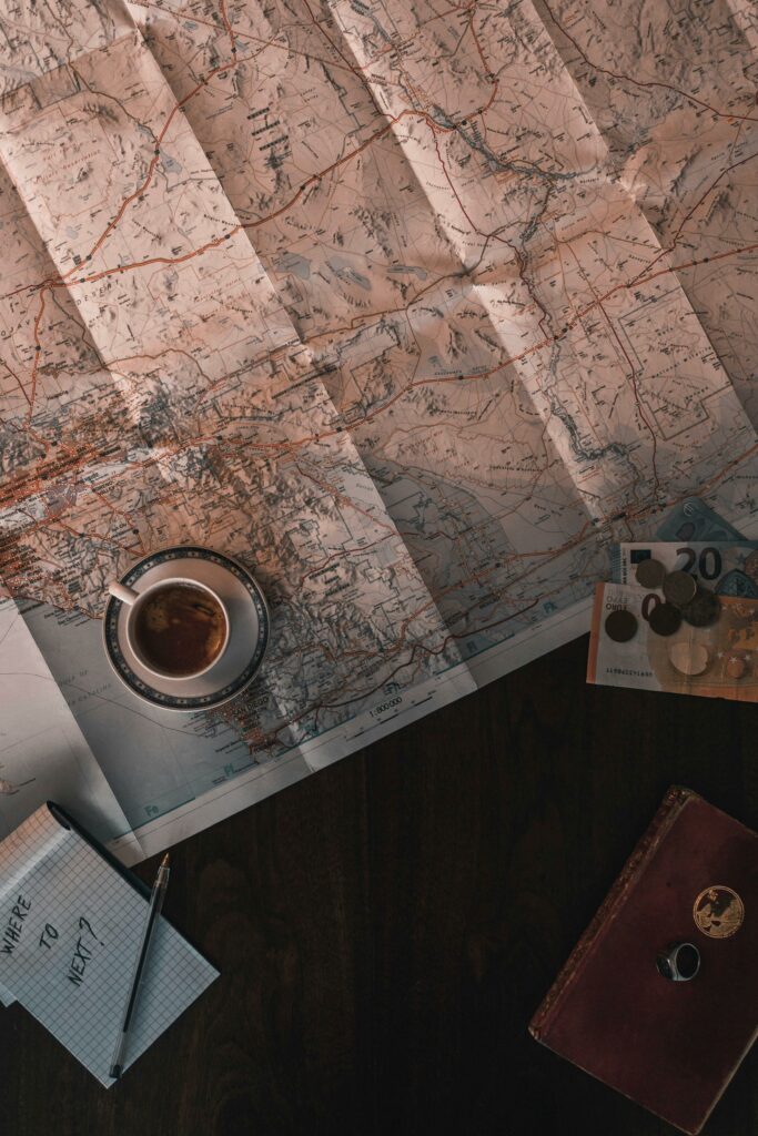 Flat lay of map, coffee, coins, and notebook for travel planning.